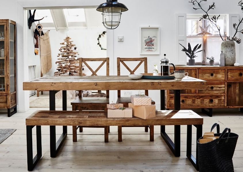 Industrial reclaimed wood dining table with matching wooden bench and Christmas tree in background