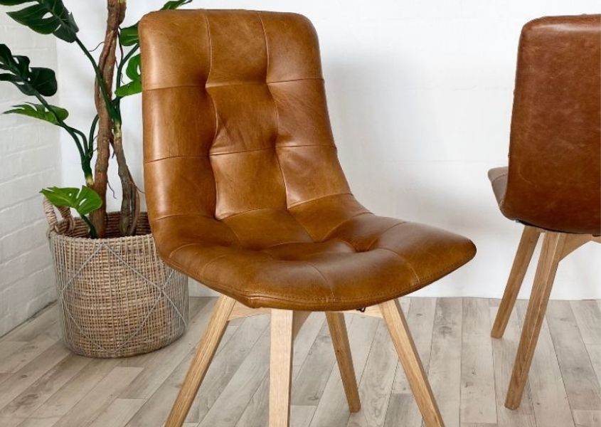 Tan leather dining chair with wooden legs and floor plant in background