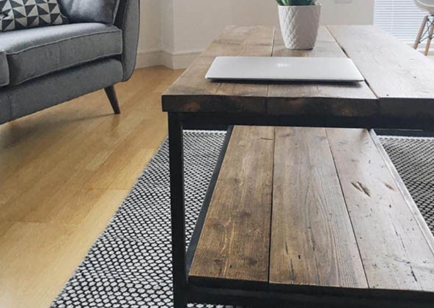 Industrial reclaimed wood coffee table on grey rug with sofa in background