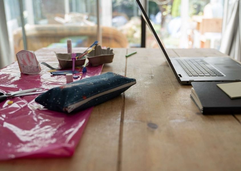 Rustic wood dining table with laptop and pencil case on top