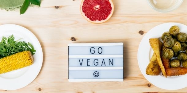 Go Vegan box-light sign on pale wood table with plates of vegetables and half a grapefruit