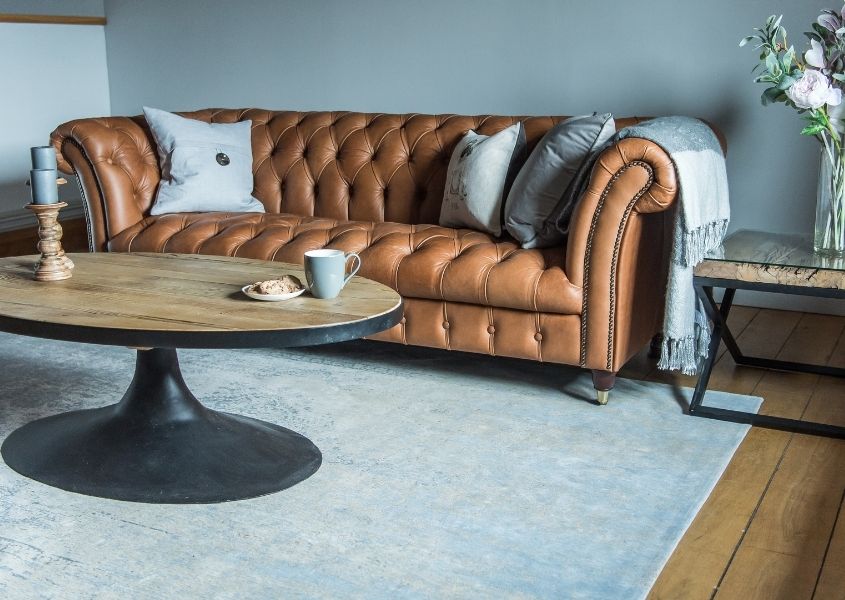 Brown leather chesterfield sofa against blue wall with oval coffee table on light blue rug
