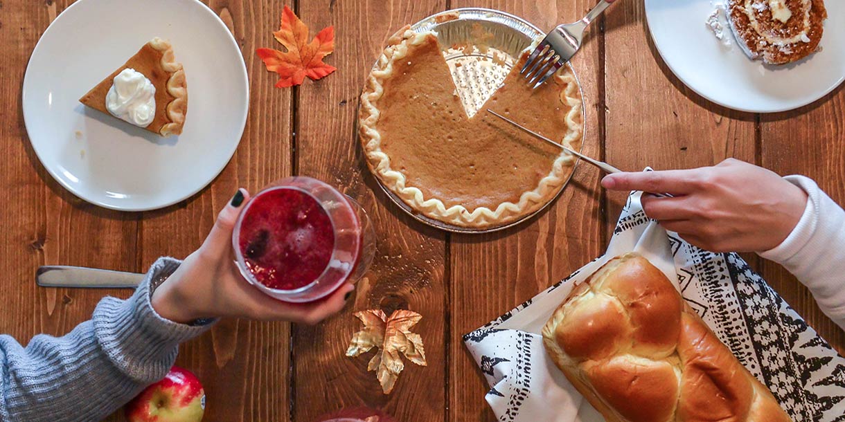 Pumpkin pie and a loaf of bread on a rustic dining table with two people around the table