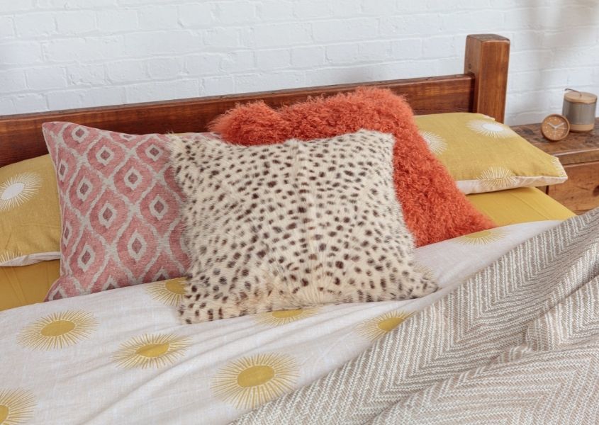 Orange, yellow and animal print cushions on wooden bed