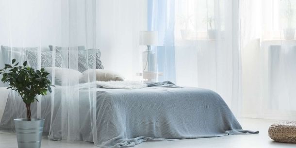 Large bed with grey covers and white sheer curtains and drapes