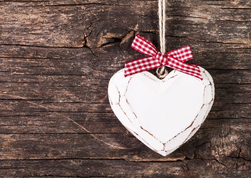 White wooden heart with red bow on rustic wood