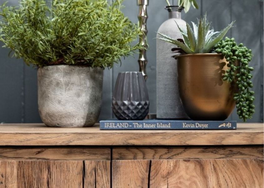 Green plants in stone pots on wooden sideboard for how to bring the outdoors in