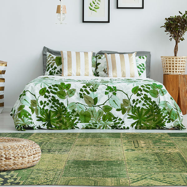 Green rug with a wicker pouffe in front of a bed with green plant-printed bedding