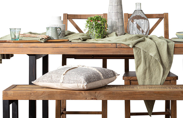 Rustic wood dining table on black steel legs with light green table linen, a grey pillow and ceramics