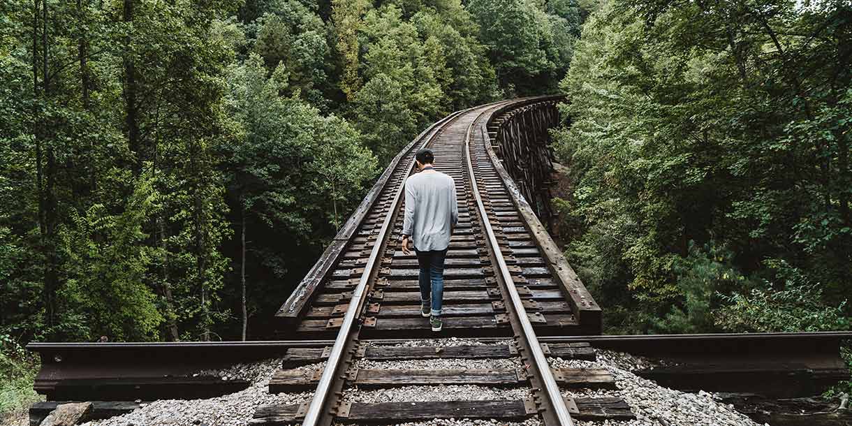 Man walking on wooden railway in the middle of a forest