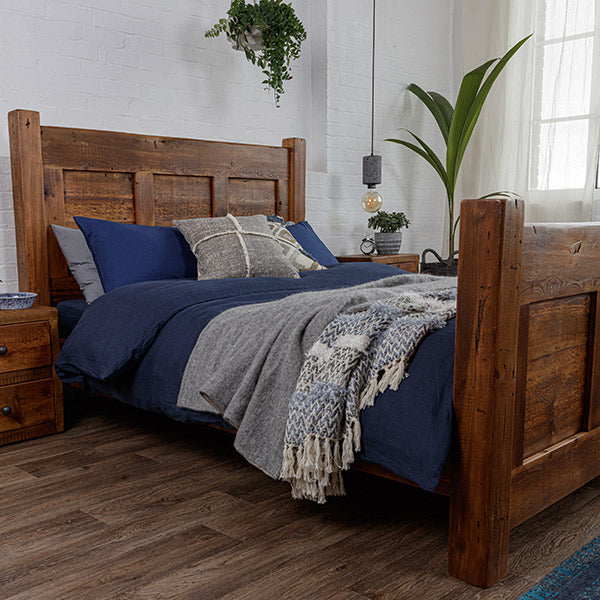 Dark reclaimed beam bed and bedside table, with navy blue and grey duvet covers and blankets and greenery
