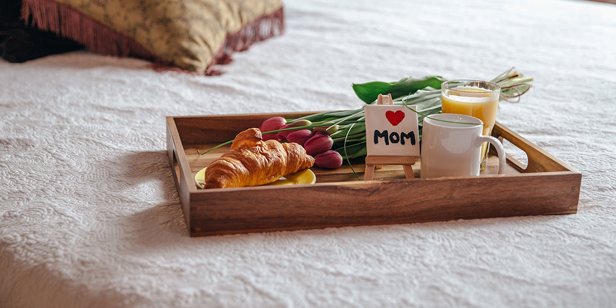 A wooden tray with a croissant and flowers on top of a bed