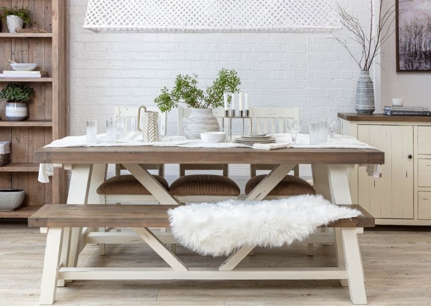 Reclaimed wood trestle dining table with white painted legs, matching wooden bench with white faux fur throw on top