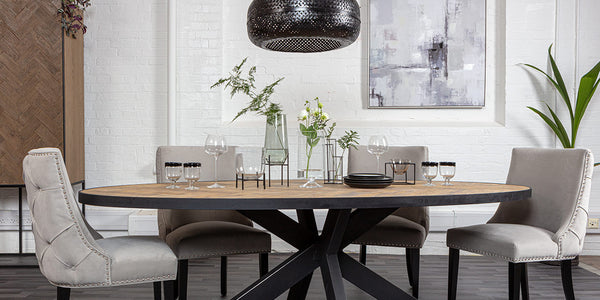 Luxe dining room with light grey button back dining chairs, spider leg industrial dining table, black rattan pendant and tableware
