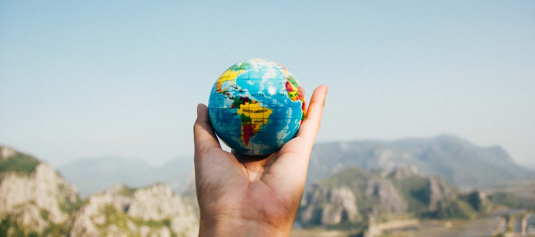 Hand holding a globe of the world against a blue sky