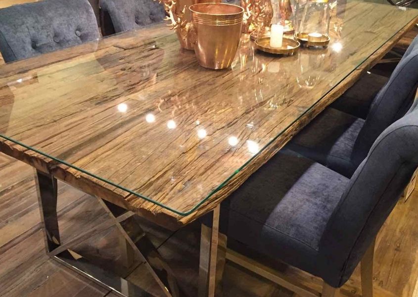 Close up of rustic reclaimed wood dining table with glass top and blue fabric dining chairs