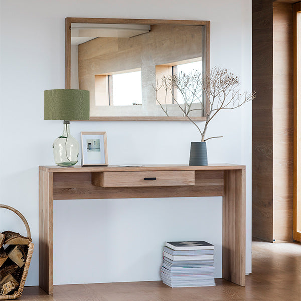 Reclaimed wooden console table in light wood with wood framed mirror hanging above and a recycled glass table lamp with a sage green shade