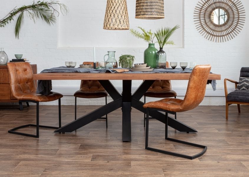 Rustic dining table with black steel spider legs, tan leather dining chairs and bamboo mirror on wall
