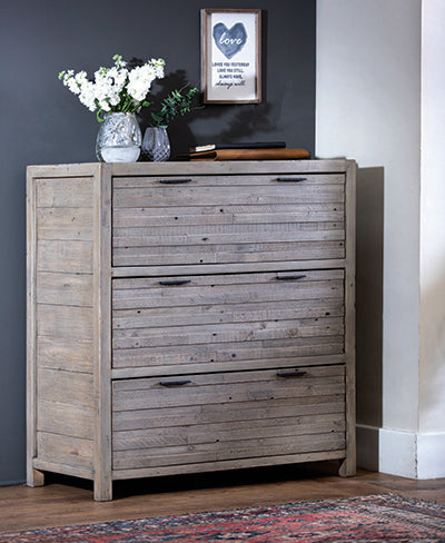 A reclaimed wood chest of drawers in a bedroom with a vase of flowers and a picture on top