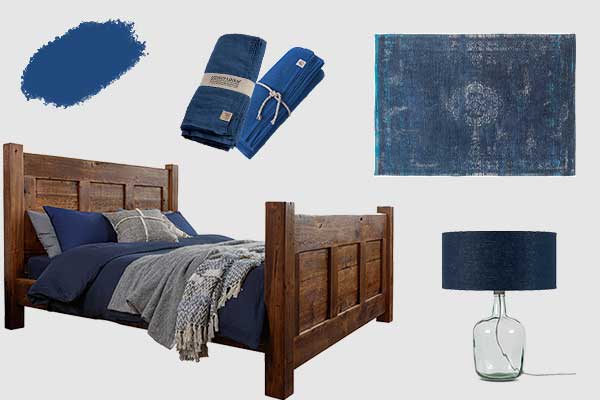 A reclaimed wooden bed with blue bedding, a blue recycled glass lamp, a blue rug and blue linen