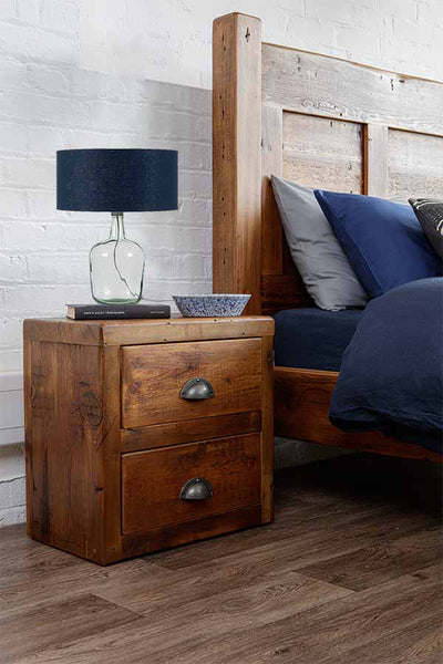 A blue recycled glass lamp on top of a rustic wooden bedside table in a bedroom
