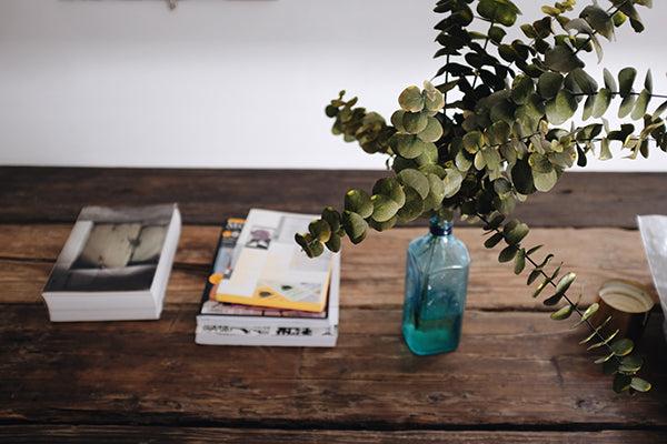 Books and a vase with eucalyptus on top of a rustic wooden surface