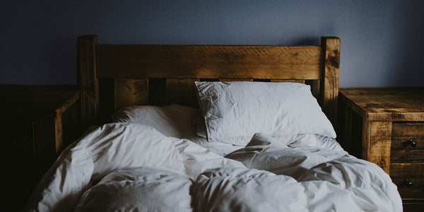A rustic wooden bed in a bedroom with soft blue walls and white bedding