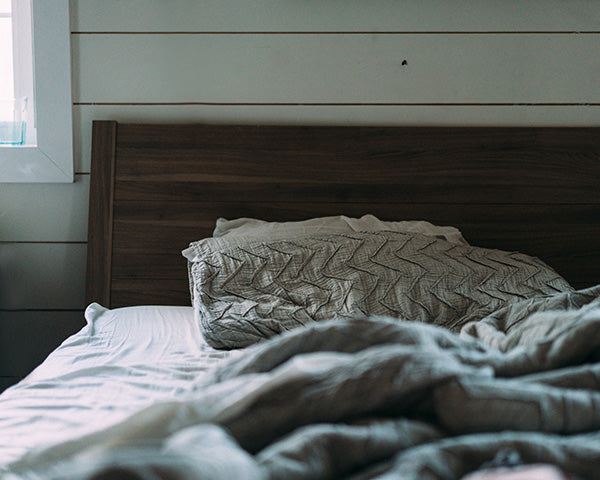 A pillow and bedding in an unmade wooden bed
