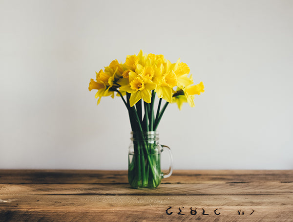 A bouquet of yellow flowers in a mason jar on top of a rustic wooden surface