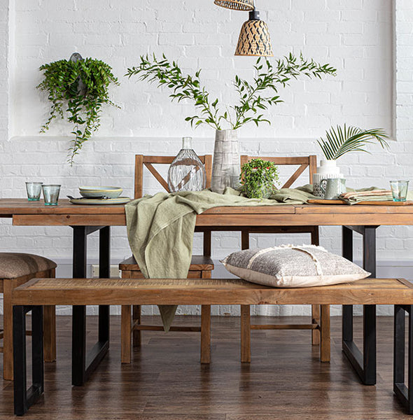 Reclaimed wood dining table dressed with sage green linen and plants, accompanied by an industrial style dining bench