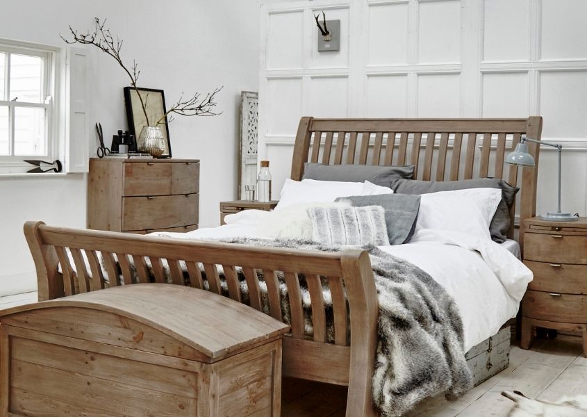 White bedroom with reclaimed wood bed, blanket box and side tables with grey faux fur throw on bed