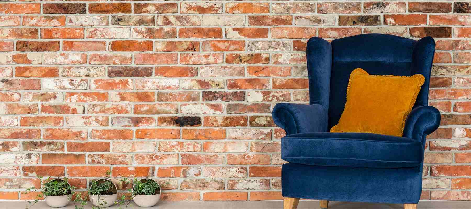 Blue velvet winged back armchair against brick wall