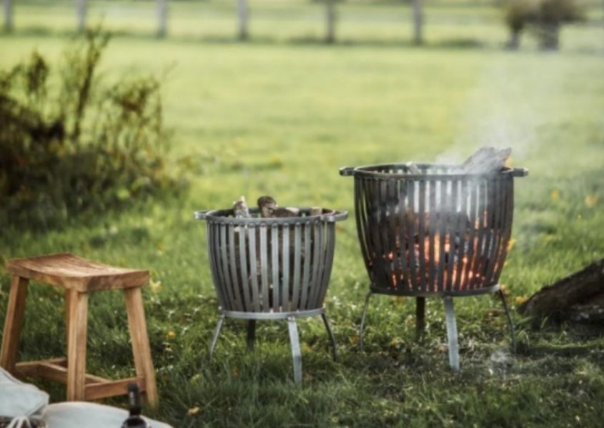 Two steel fire pits in a field with small wooden stool
