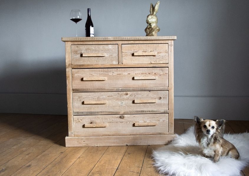 Reclaimed wood chest of drawers with small dog of sheepskin rug on the floor