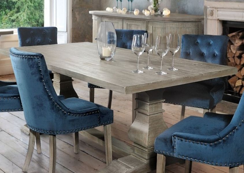 Large reclaimed wood dining table with monastery style legs and bright blue velvet armchairs