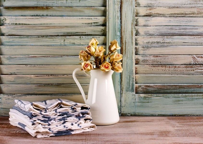 white jug with yellow flowers in front of rustic wooden shutters