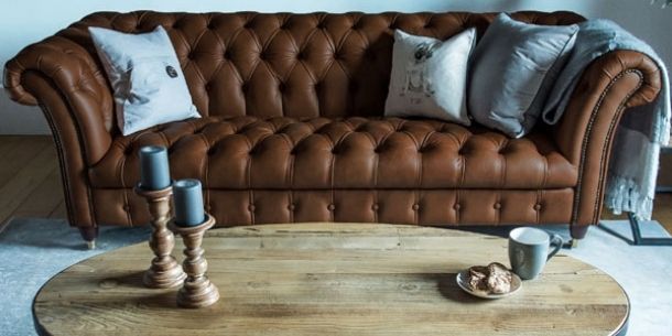 Brown leather chesterfield sofa with rustic coffee table and wooden sticks with blue candles