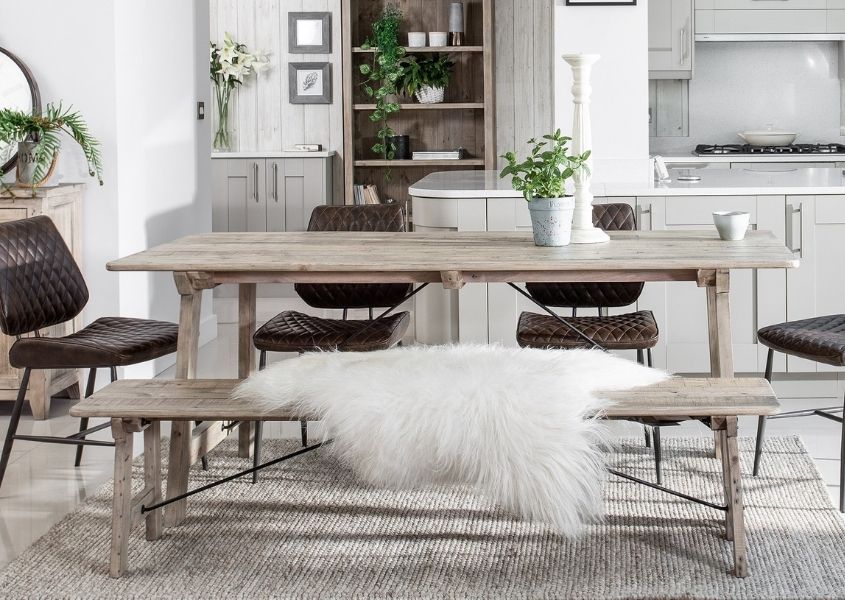 Rustic dining table with matching wooden bench with white faux fur throw and brown faux leather dining chairs
