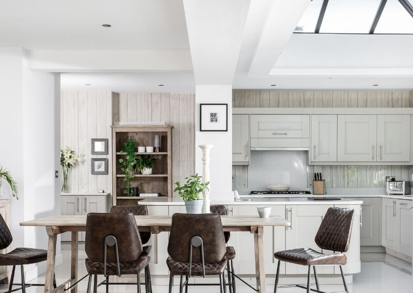 Pale reclaimed wood dining table in pale grey kitchen with brown leather dining chairs and large pitched roof skylight