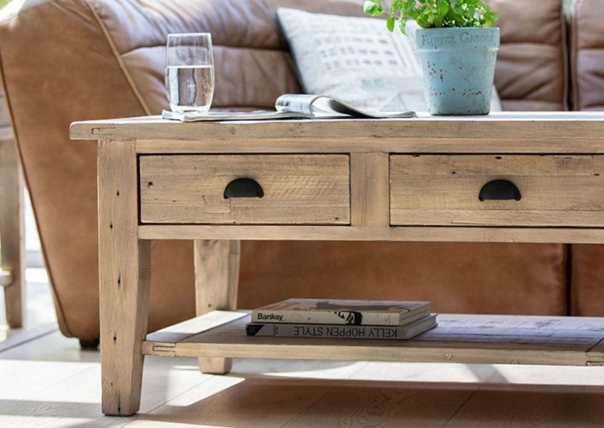 Reclaimed wood coffee table with two drawers and shelf and brown leather sofa behind