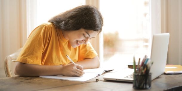 girl in yellow t-shirt writing at a desk