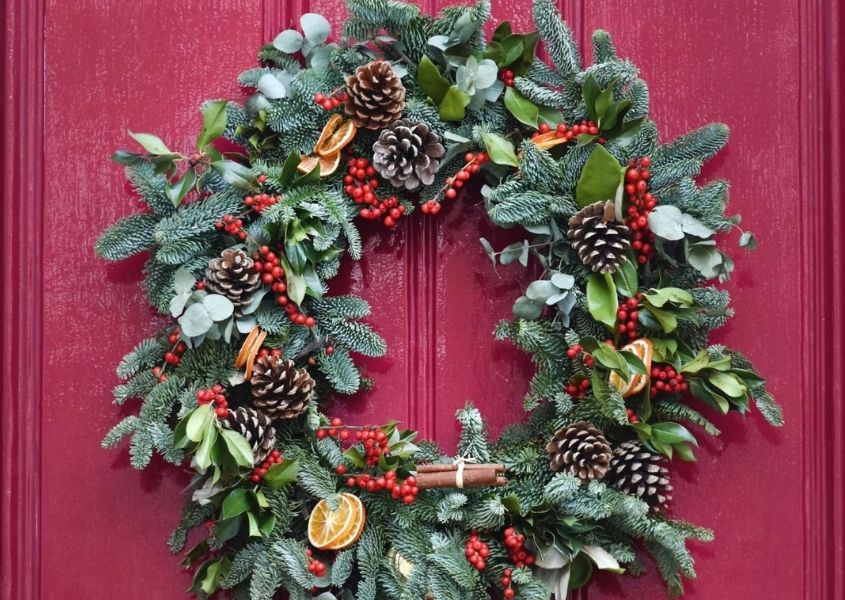 Christmas wreath made with pine leaves, cones & berries hanging on bright pink door