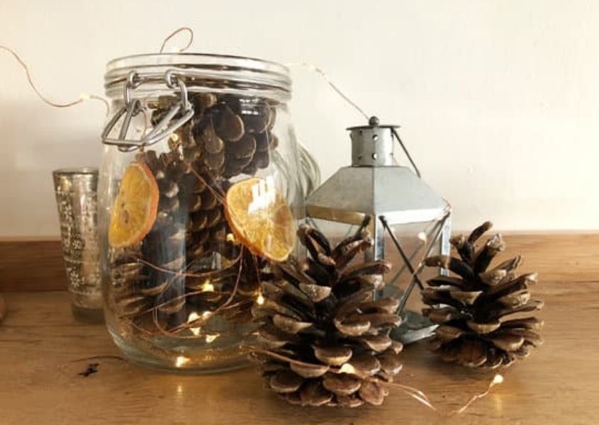 Glass jar filled with pinecones, dried orange slice and fairy lights