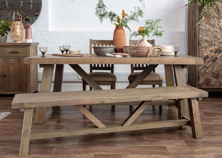 Reclaimed wood dining table with trestle legs and matching wooden dining bench styled with a terracotta vase and green plant