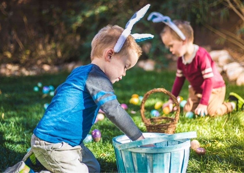 Two children wearing bunny ears in a garden having an Easter Egg hunt
