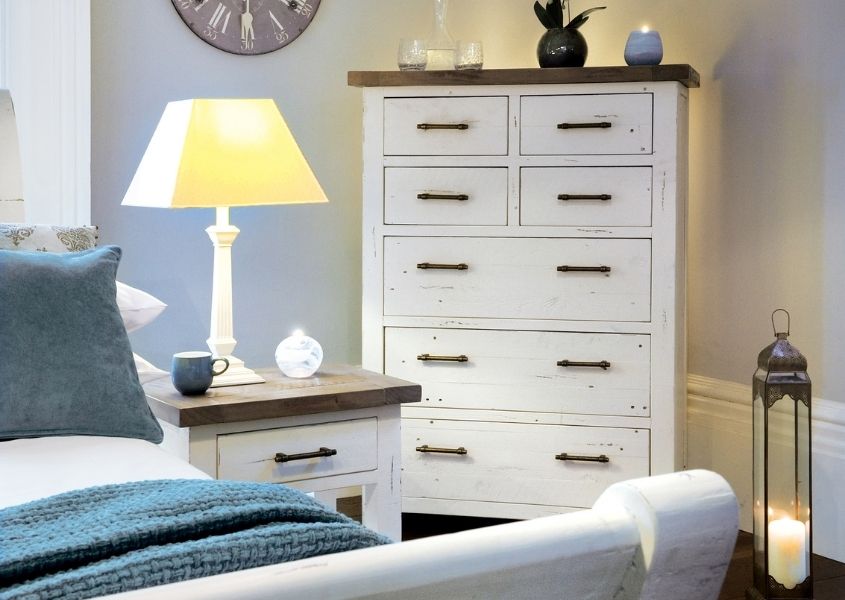 Tall white chest of drawers next to matching small bedside table and white wooden bed