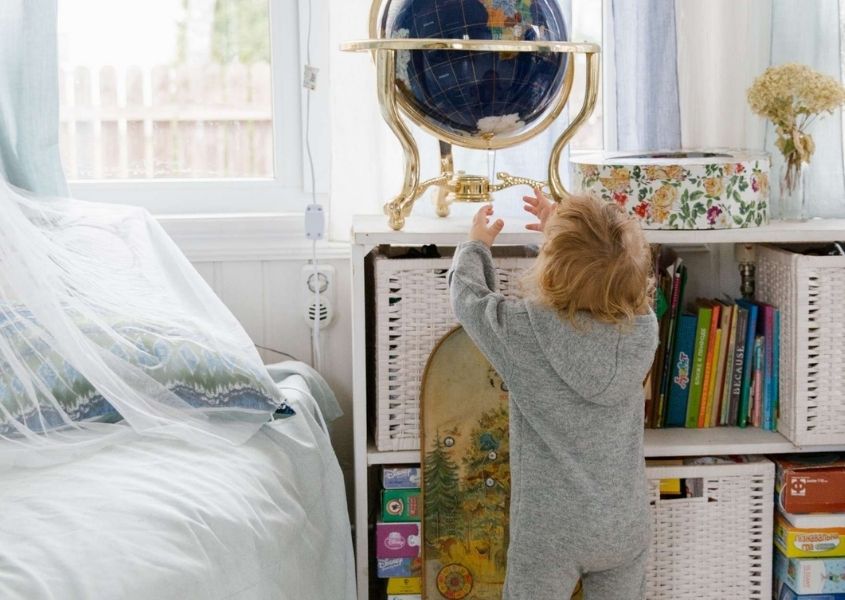 Small child reaching for a decorative globe of the earth on white rustic shelves