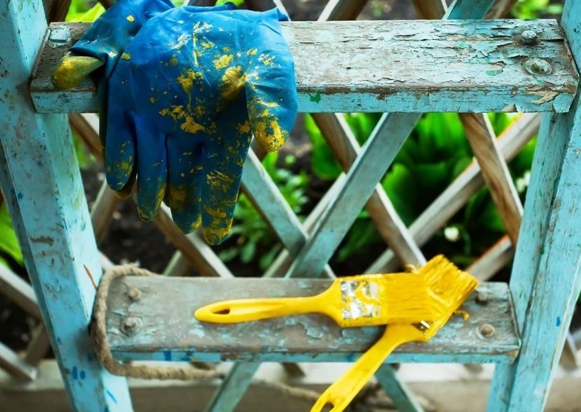 Yellow paintbrushes and blue glove on a distressed blue painted wooden ladder
