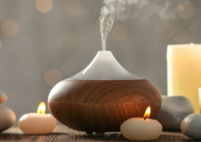 Wooden essential oil diffuser with steam coming out of the top, surrounded by white candles