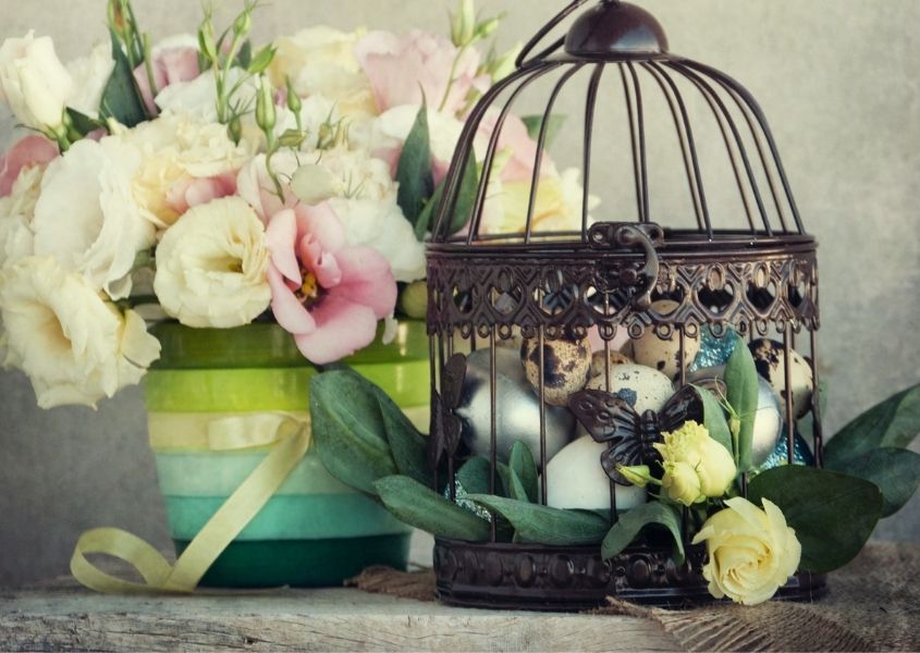 vintage bird cage filled with pained eggs on rustic dining table